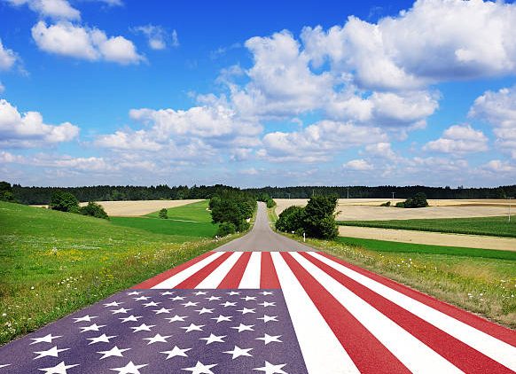 Country road with American flag, blue sky with white clouds.