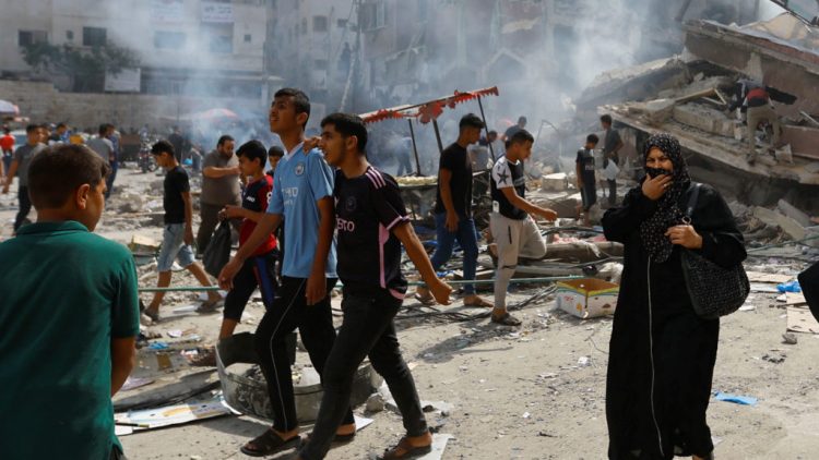 Palestinians walks near the rubbles in the aftermath of Israeli strikes