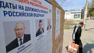 A man walks past an information board with portraits of Russian presidential candidates in the upcoming election in Yevpatoriya