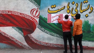 Iranian men put campaign posters on a wall during the last day of election campaigning in Tehran
